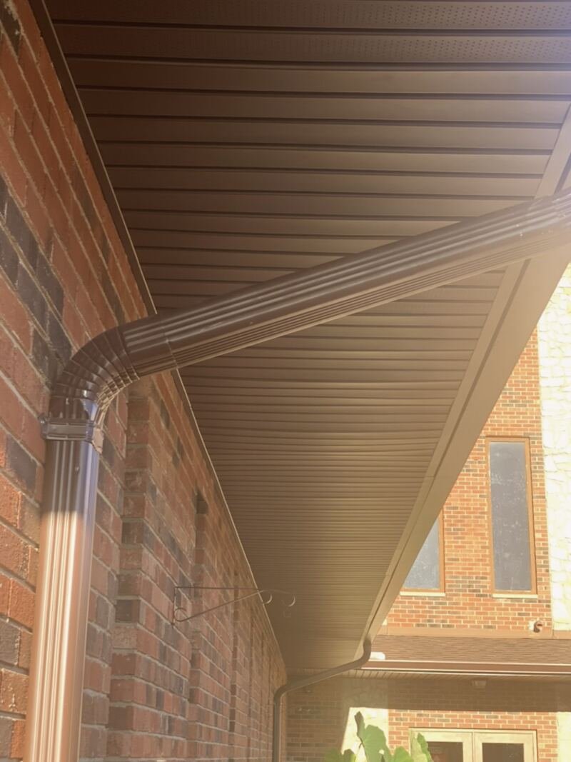 Brown seamless gutter and downspout under a new soffit on a brick house