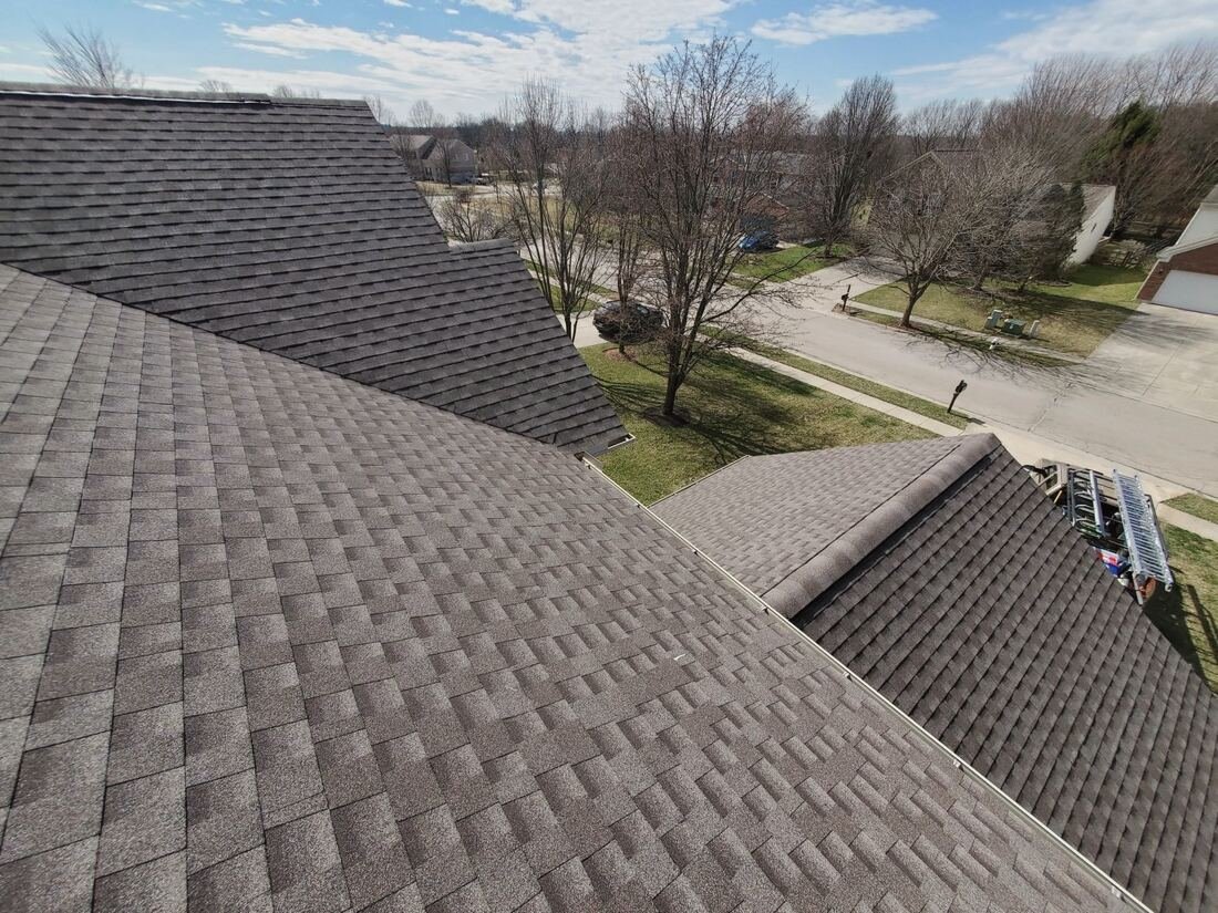 New dark grey architectural shingles on a two-slope roof, neighborhood in the background