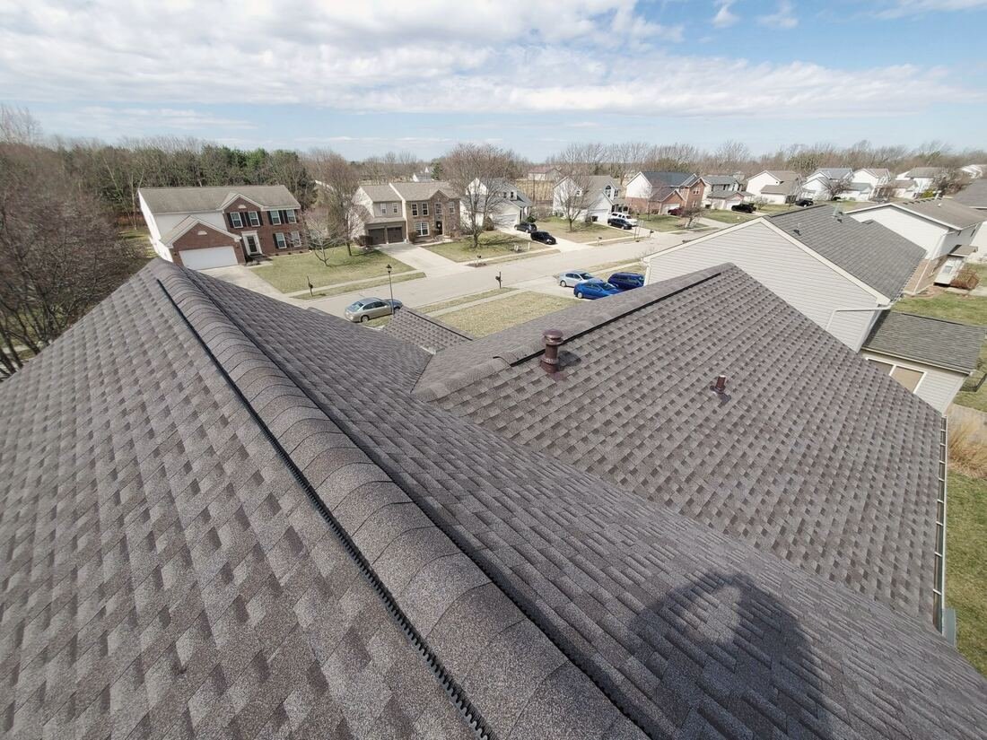 View from a roof ridge over new grey shingles and a ridge vent, houses and street below