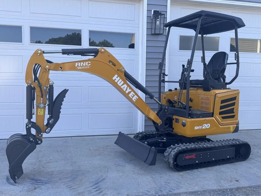 Orange Huayee SHY20 mini excavator with canopy and bucket tucked in, on a concrete pad by garage doors