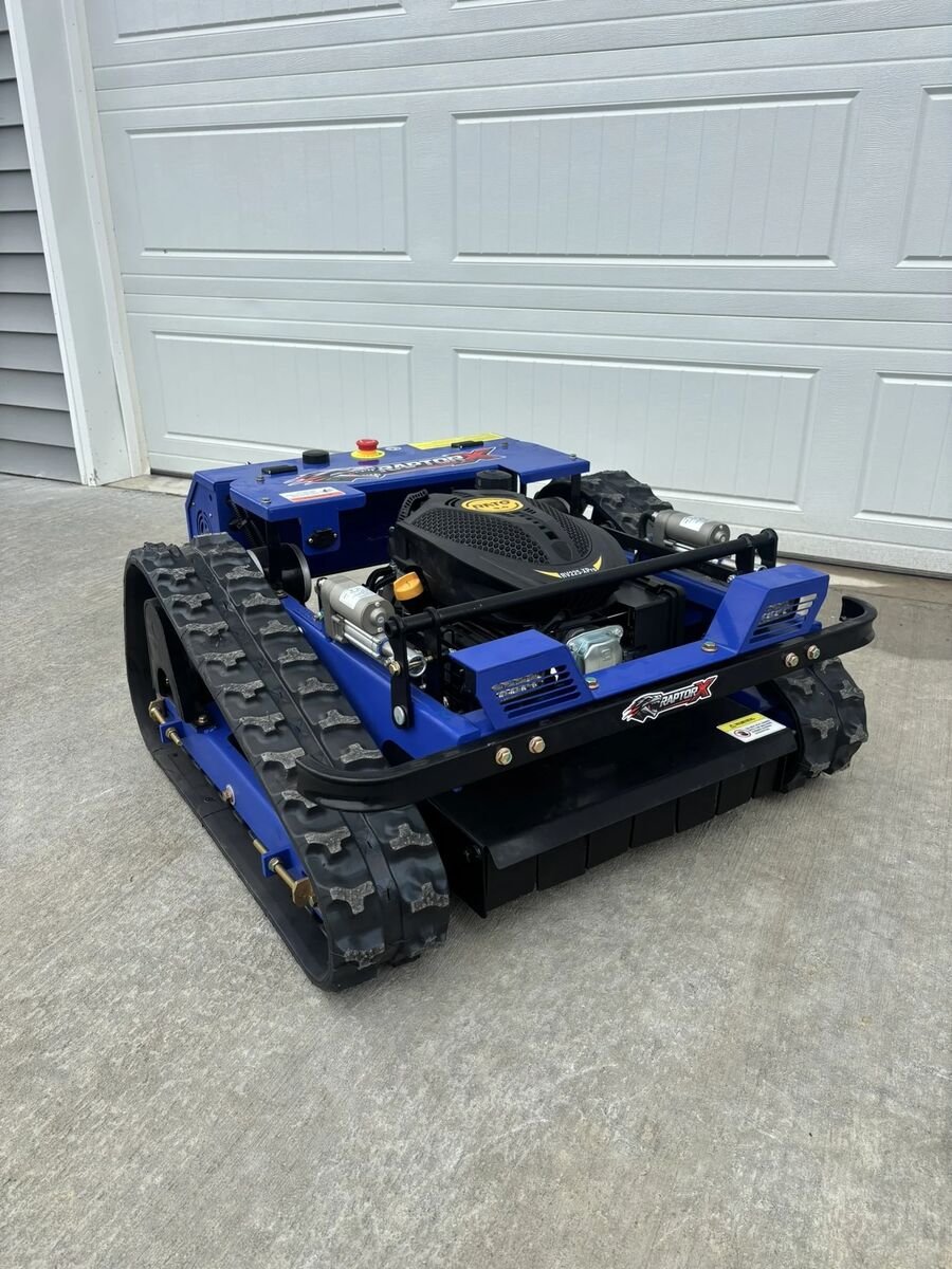 Blue and black tracked remote control mower with the engine exposed, on a concrete pad