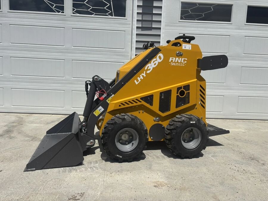 Orange Huayee LHY360 wheeled mini skid steer with a bucket, parked by garage doors