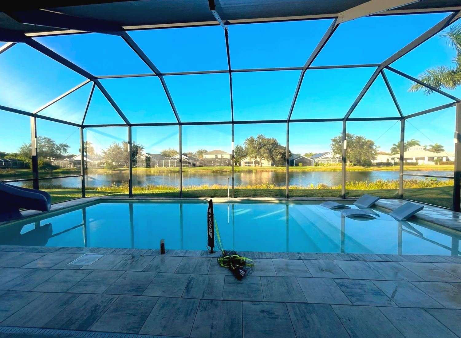 Pool cage on a lake at golden hour, clear sky through the screen, gray tile deck in the foreground
