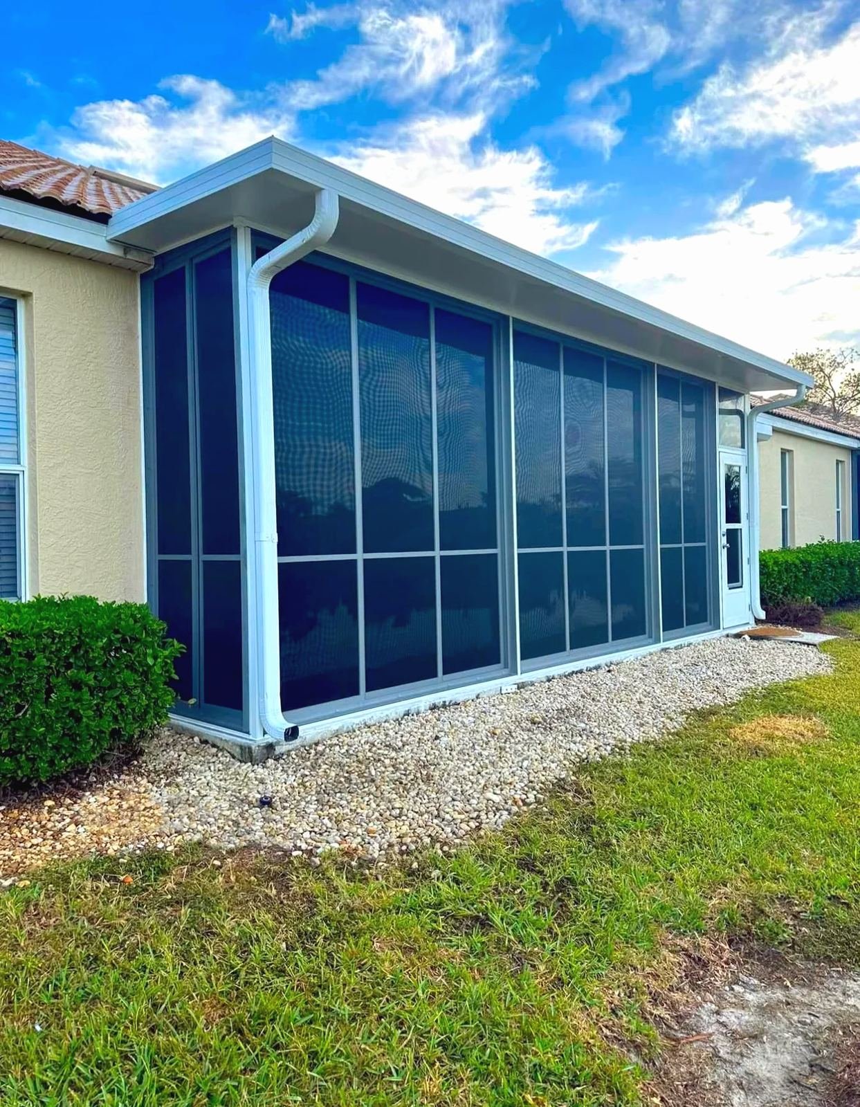 White aluminum screen room with a solid roof and dark tinted panels on the back of a stucco house, blue sky with clouds, Southwest Florida