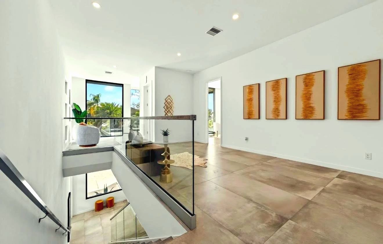 Frameless glass railing around a stair opening in a modern interior with wood-look tile floors and four framed prints on the wall