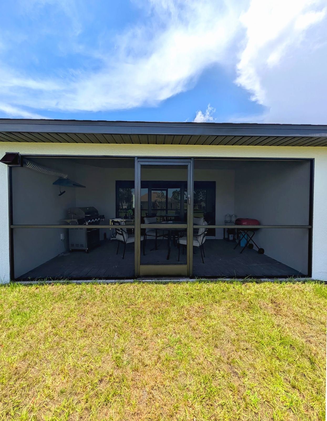 Bronze-framed screened lanai under an existing roof, grill and table inside, dry lawn in front, Southwest Florida
