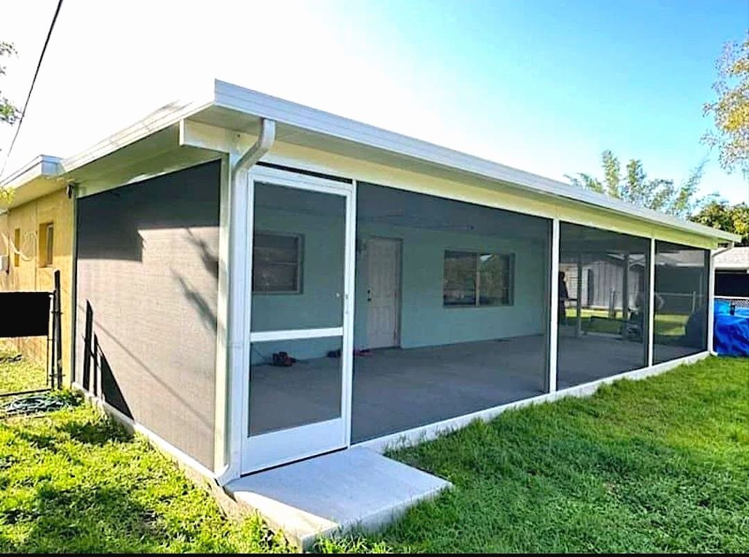 Long white-framed screened lanai with a solid roof along the back of a house, screen door at the near end, green lawn