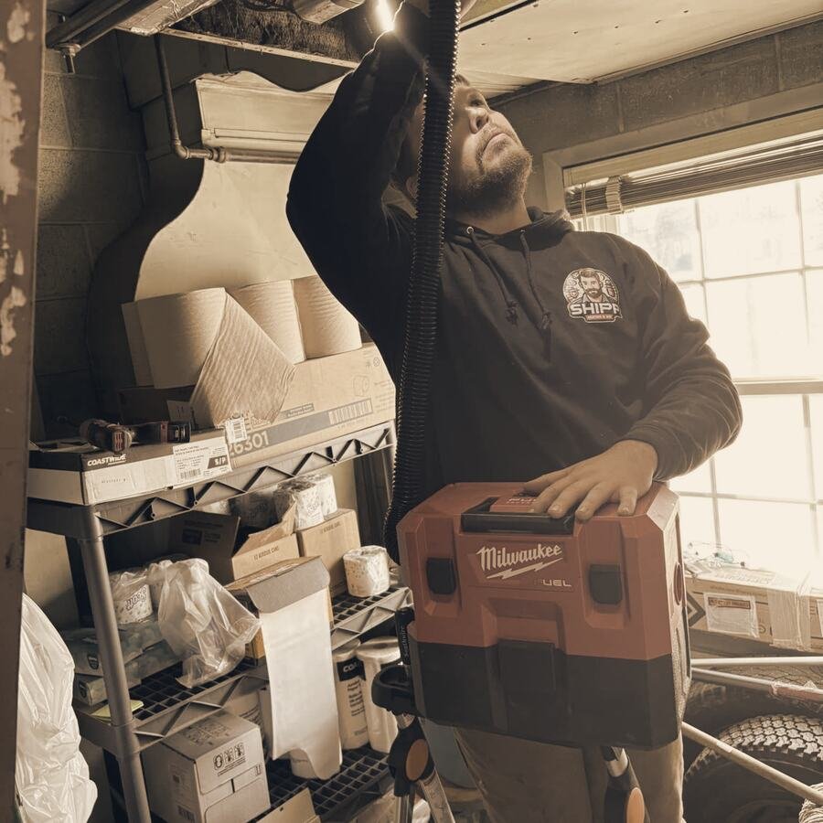Shipp's tech in a SHIPP hoodie vacuuming out a ceiling duct