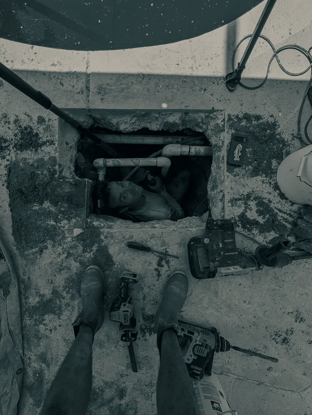 Overhead view of a Splash technician working in an excavation opened beneath a pool deck to reach the leaking line